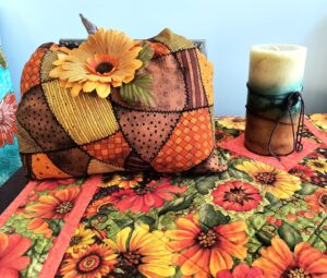 Fabric pumpkin and candle sit on a table runner